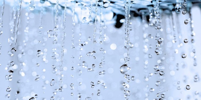 Wassertropfen fallen in einer sanften Bewegung, während sie im Licht funkeln und eine ruhige Atmosphäre schaffen.