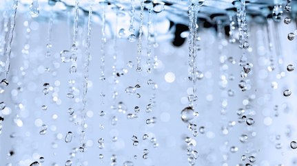 Wassertropfen fallen in einer sanften Bewegung, während sie im Licht funkeln und eine ruhige Atmosphäre schaffen.