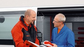 Ein Vissmann Mitarbeiter zeigt einem Kunden, einen Ordner vor einem Firmenbulli