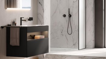 Ein modernes Badezimmer mit einem eleganten schwarzen Waschbecken und einem großen Spiegel, der sanft beleuchtet ist.