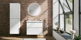 Ein modernes Badezimmer mit einer weißen Waschtischkommode und einem runden Spiegel vor einer Backsteinwand.