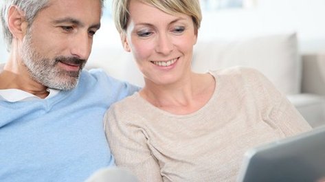 Ein Paaerchen sitzen nebeneinander und schauen auf ein Tablet