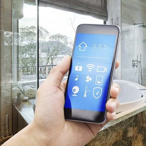 Badezimmer mit einer Hand die ein Smartphone hält, die eine Steuerung einer Lueftung-Klima-App zeigt.